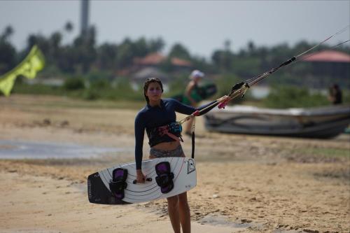 a woman walking on the beach holding a surfboard at De Silva Palm Resort in Kalpitiya