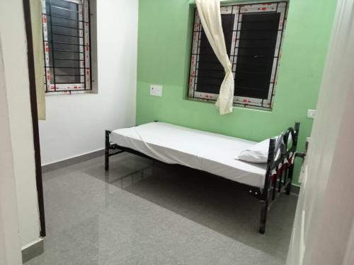 a small bed in a room with two windows at Allamanda Abode in Chennai