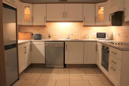 cocina con armarios blancos, fregadero y lavavajillas en Millstone Cottages, en Milford