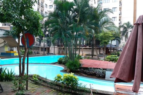 a swimming pool with palm trees and an umbrella at Apartemen Paragon Village by CV Kita Property & Partner in Tangerang