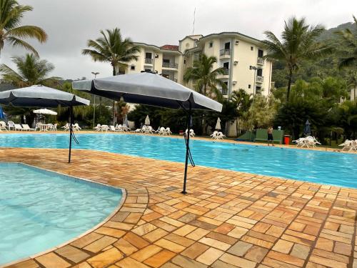 uma piscina com dois guarda-sóis ao lado de um hotel em Apto Condomínio Wembley Tênis em Ubatuba