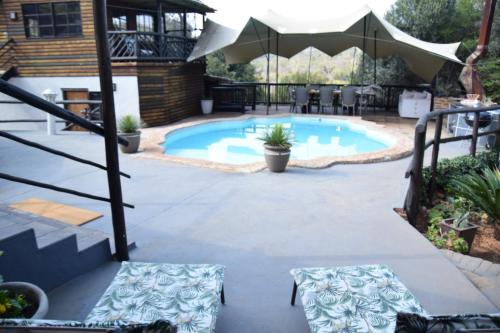 a patio with a pool with chairs and an umbrella at Khululeka Guest Farm in Millvale