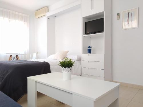 a white bedroom with a white table and a tv at Apartamentos Pagán in Santiago de la Ribera