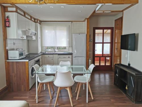 uma cozinha com uma mesa de vidro e cadeiras brancas em Casita independiente con jardín y chimenea. em Cercedilla