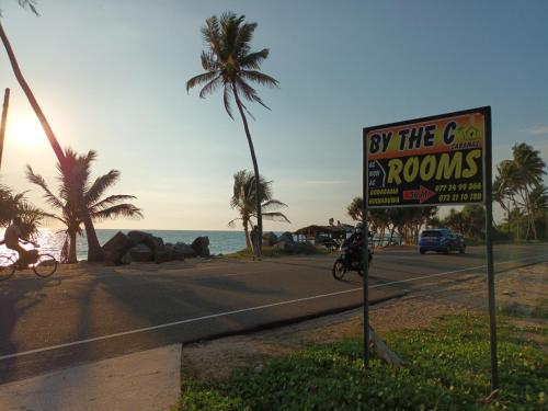 a sign for by the rooms on a road next to the ocean at By The C' Cabanas in Hikkaduwa