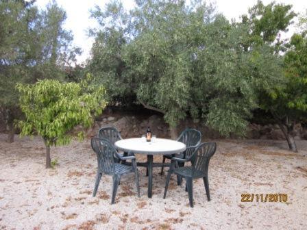 a table and chairs sitting on the sand near trees at Bungalow with 2 double bedrooms in the hills . in Akoursos