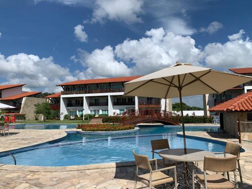 uma mesa com um guarda-sol ao lado de uma piscina em Flat no Club Meridional de Carneiros - Bloco 4-2PP em Tamandaré