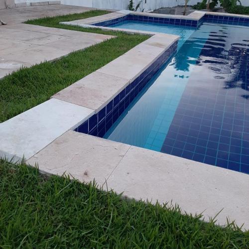 a swimming pool with blue tiles in the grass at Casa Vitória em barra de jacuipe in Campos