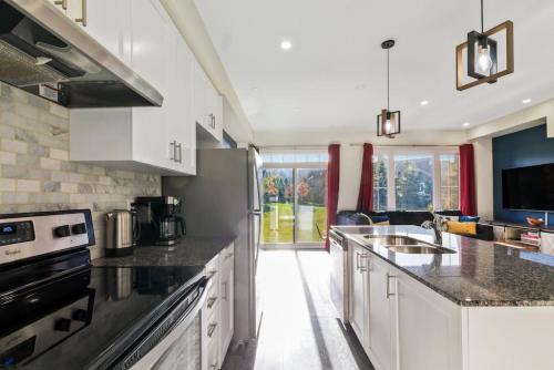 a kitchen with white cabinets and black counter tops at Modern home with a pool sauna pooltable & mountain view in Collingwood