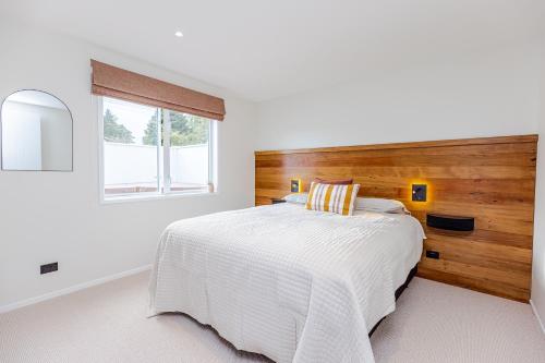 a white bedroom with a large bed with a wooden headboard at Rata Boutique Apartments in Ohakune