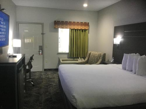 um quarto de hotel com uma cama grande e uma cadeira em Muskogee Inn and Suites em Muskogee