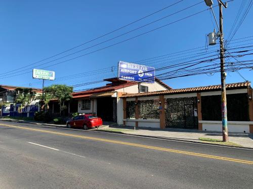 a red car parked in front of a building on a street at Berlor Airport Inn in Alajuela City