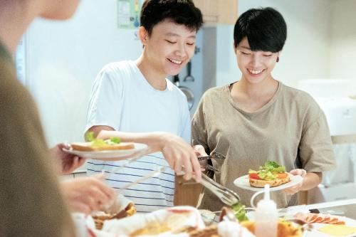 a group of people standing around a table with plates of food at Hostel Tomato 番茄溫泉青旅 in Jiaoxi