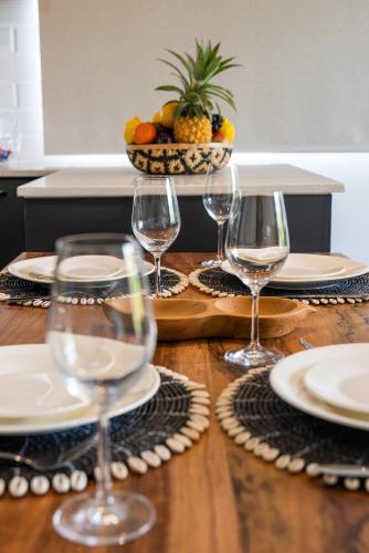 a wooden table with wine glasses and plates on it at 373 Wolmar Cosy and Modern Apartment- 200 metres from the Beach and Supermarkets and just next to Domaine de wolmar with views of deers and green natural park in Flic-en-Flac
