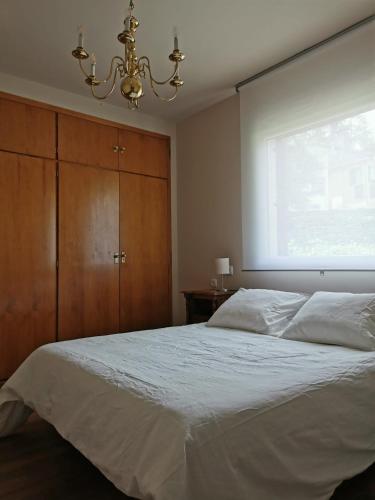 1 dormitorio con cama blanca y lámpara de araña en Casita independiente con jardín y chimenea., en Cercedilla