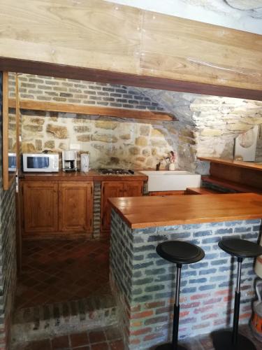 une cuisine avec un mur en pierre et un comptoir avec des tabourets dans l'établissement Ardèche les cigales, studio murier piscine partagée, à Grospierres