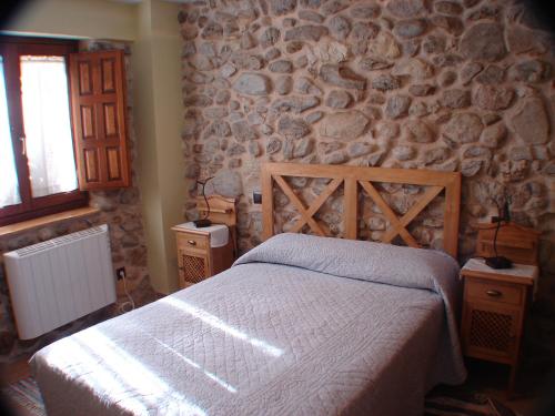 a bedroom with a bed and a stone wall at El Refugio de la Sauca in Alameda del Valle