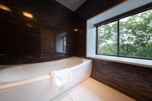 a bathroom with a bath tub and a window at 伊豆高原温泉ホテル 森の泉 in Ito