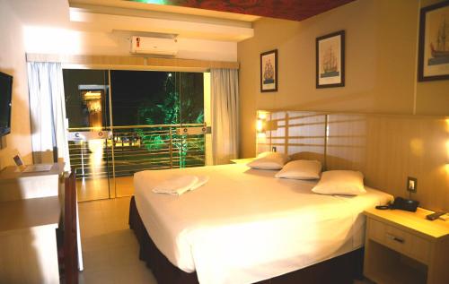 um quarto com uma grande cama branca e uma janela em Hotel Colombo em Barra do Garças