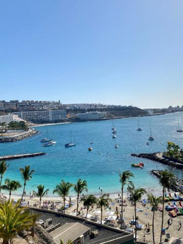 a view of a beach with palm trees and boats at Lovely apartment seaview in Puerto Rico with heated swimming pool, free Wi-Fi and free private parking in Puerto Rico de Gran Canaria