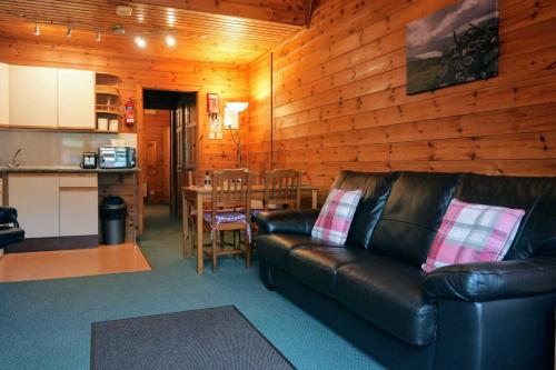 a living room with a leather couch and a kitchen at Woodland Spruce Lodge in Killin