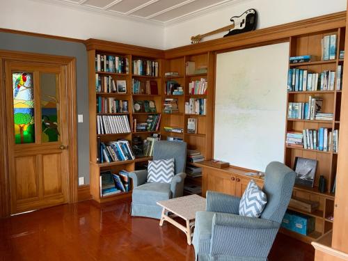 a library with two chairs and a table and bookshelves at Glenfern Sanctuary in Port Fitzroy