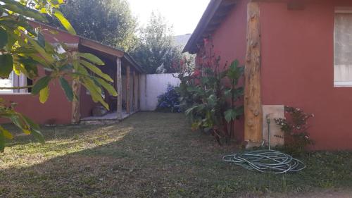 a yard next to a red house with a hose at Cabañas Las Acacias in San Clemente del Tuyú