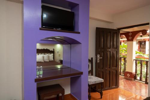 a bedroom with a purple wall with a tv above a fireplace at Hotel D’Monica in San Cristóbal de Las Casas