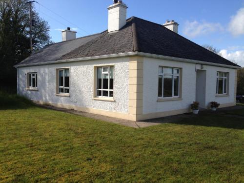 una casa blanca con techo negro en un patio en Pat's Cottage, en Kinawley