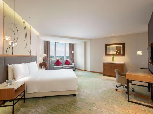 a hotel room with a large white bed and a desk at Radisson Golf & Convention Center Batam in Batam Center