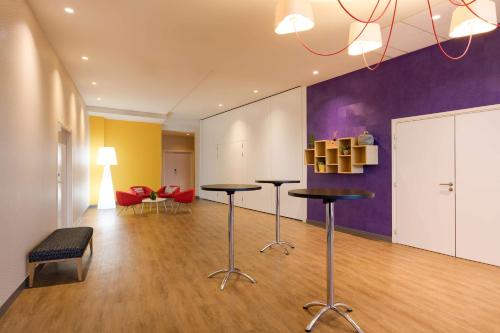 un salon avec deux tables et un mur violet dans l'établissement Park Inn by Radisson Lille Grand Stade, à Villeneuve d'Ascq