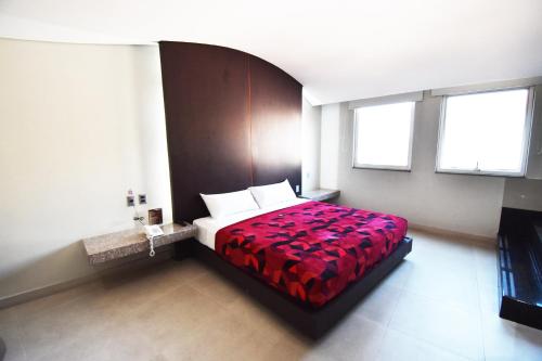 a bedroom with a bed with a red bedspread and two windows at Hotel Via La Villa in Mexico City