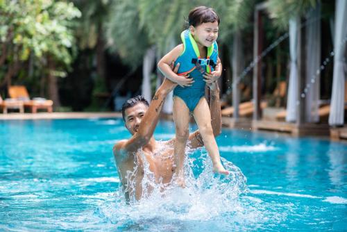 a man holding a little girl on his back in a swimming pool at Palace Gate Hotel & Resort By EHM in Phnom Penh