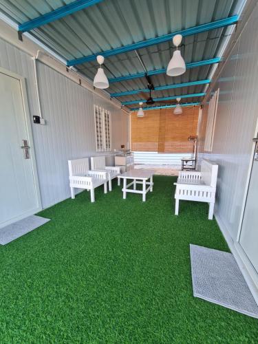 a covered patio with white benches and green grass at Cheqma Tiny Chalet in Kota Bharu