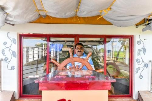 a man sitting on a boat with a steering wheel at Beach Paradise Day Cruise Houseboat in Alleppey