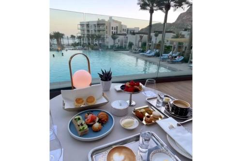 a table with breakfast food next to a pool at Apartment the address resort- Two-Bedroom and maid room in Al Aqah