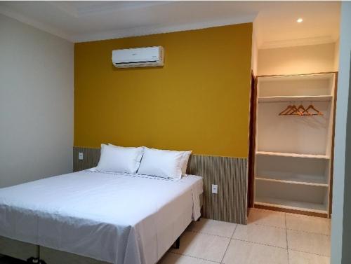 a bedroom with a white bed and a yellow wall at Pousada Império in São Miguel do Gostoso