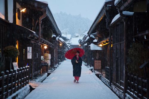 a woman walking down a street with a red umbrella at Honjin Hiranoya Kachoan in Takayama