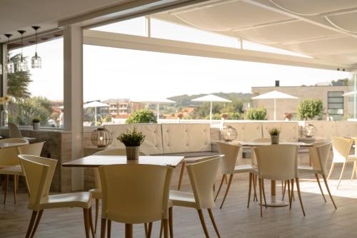 un restaurante con mesas y sillas blancas y ventanas en Hotel Piramide, en Portonovo