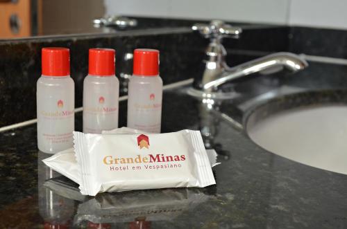 a bathroom counter with three bottles of shampoo and a sink at Hotel Grande Minas in Vespasiano