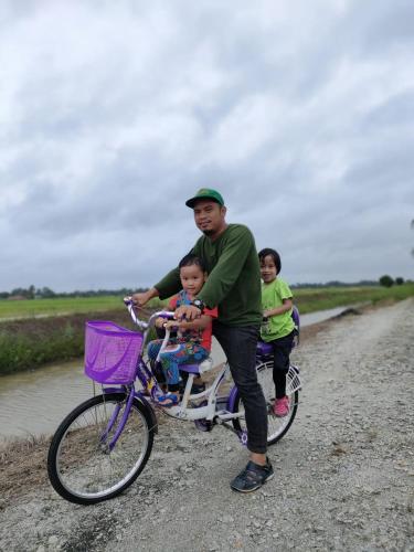 a man with two children on a bike on a dirt road at Izz Homestay Sawah Padi Sungai Besar ! in Kampong Parit Ten