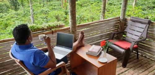 a man sitting at a table with a laptop on a porch at LAZY DAYS Wayanad in Cherambādi
