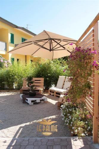 a patio with an umbrella and benches and a bush at Le Palme Holidays in Palmadula