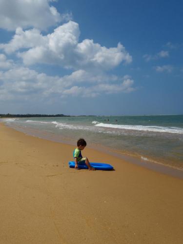 a young child sitting on a surfboard on the beach at Wellé Wadiya Beach Villa in Kalpitiya