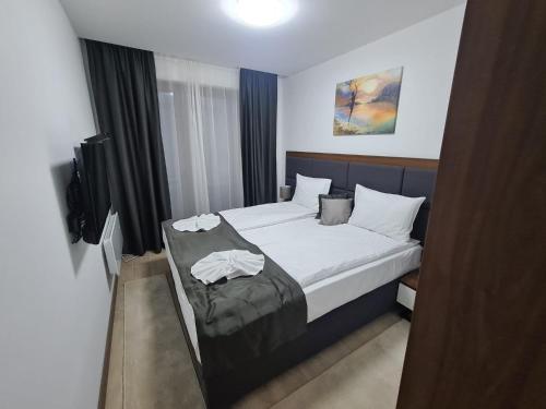 a bedroom with a bed with white sheets and a television at MK Apartments Zoned 2 Spa&Wellness in Cajetina