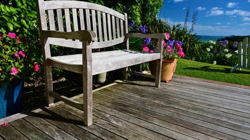 a wooden bench sitting on a wooden deck with flowers at Kākā Ridge Retreat Luxury Cottage in Tawharanui