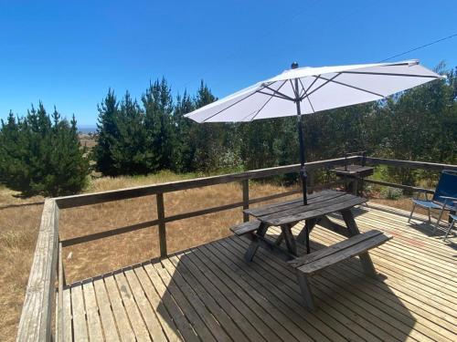 une terrasse en bois avec une table de pique-nique et un parasol dans l'établissement Cabañas Refugio Las Conejas, à Pelluhue