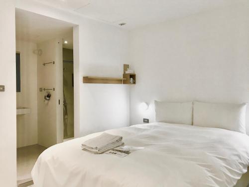 a white bed in a white bedroom with a towel on it at Norden Ruder Hostel Taichung in Taichung