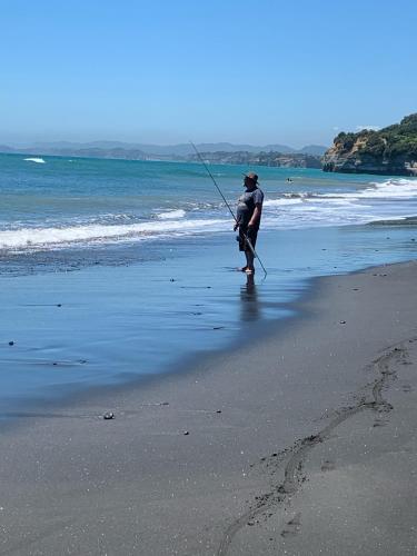 a man standing on a beach holding a fishing pole at Urenui Beach Bach in Urenui