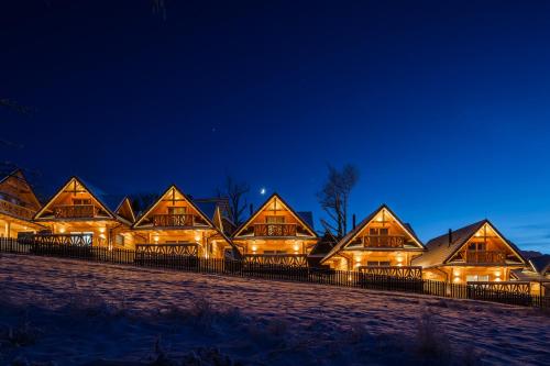 a row of wooden homes lit up at night at Osada Chłabówka Zakopane & SPA in Zakopane